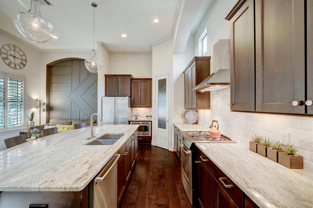This modern kitchen features elegant dark wood cabinets, a spacious granite island with seating, and stainless steel appliances. It offers ample natural light, a cozy breakfast nook, and stylish pendant lighting for a warm, inviting atmosphere.