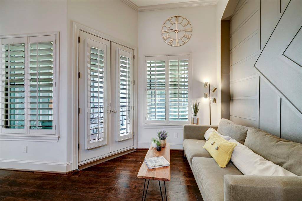 Bright living area with elegant French doors and plantation shutters, featuring a stylish accent wall. Cozy seating and hardwood floors create a welcoming atmosphere.