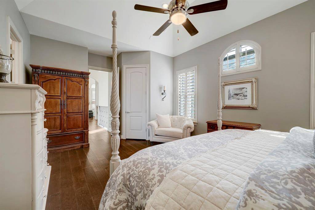 Bright and inviting bedroom with elegant hardwood floors, a cozy armchair, and ample natural light from large windows. Features a ceiling fan and classic furnishings, creating a serene, comfortable atmosphere.