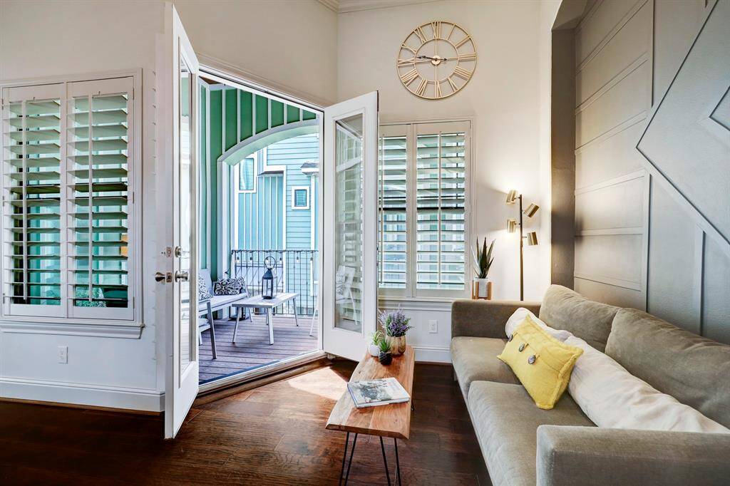 This inviting living space features elegant French doors opening to a charming balcony, perfect for relaxation. The room boasts rich wood floors, a modern accent wall, and ample natural light, creating a warm and welcoming atmosphere.