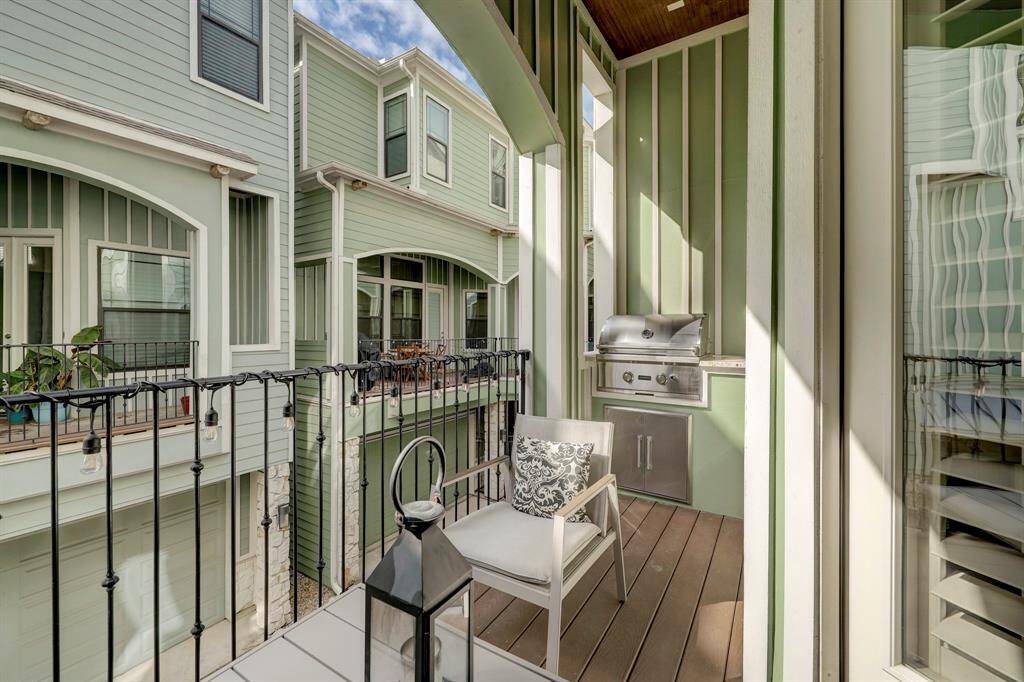 Charming balcony with a built-in grill, cozy seating, and a decorative lantern, perfect for outdoor relaxation. Surrounded by neighboring homes with a quaint architectural style.