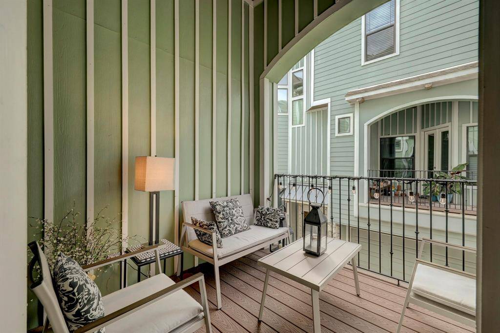 This cozy balcony features stylish outdoor seating and a table, with a soft green wall and charming views of neighboring architecture. Perfect for relaxation.