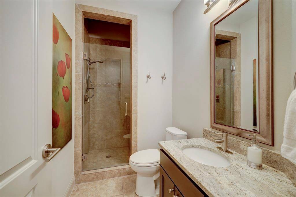 This bathroom features a modern design with a glass-enclosed shower, granite countertop, and stylish fixtures. A large mirror and tasteful artwork add a touch of elegance.