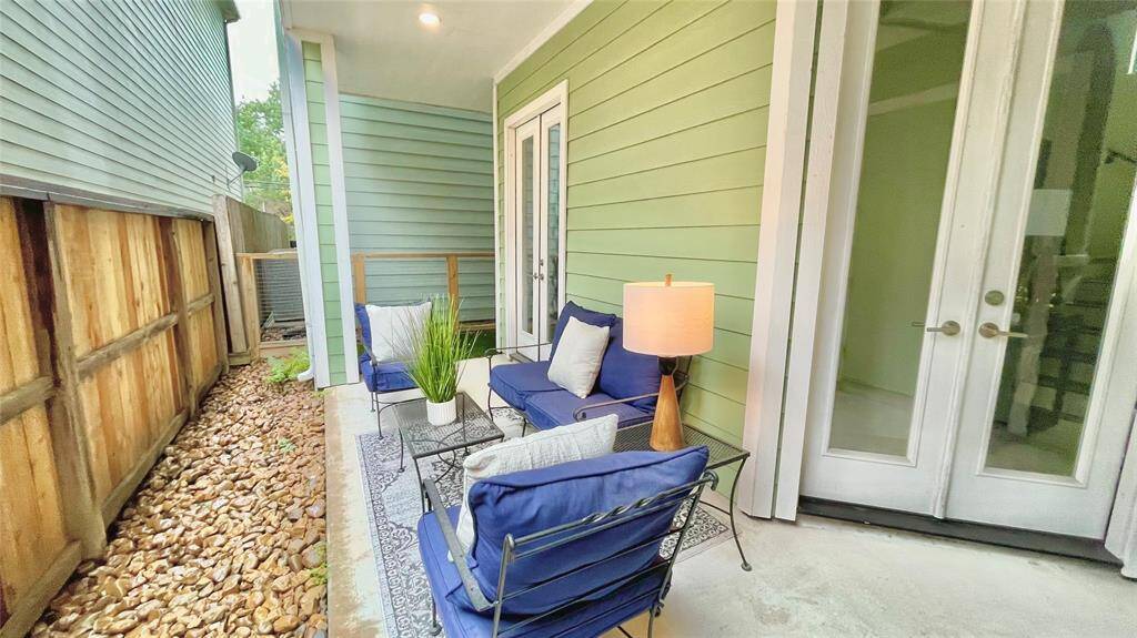 Cozy outdoor patio with green siding, featuring comfortable blue seating, a small table, and a lamp. It's a serene space for relaxation, bordered by a wooden fence and decorative stones.