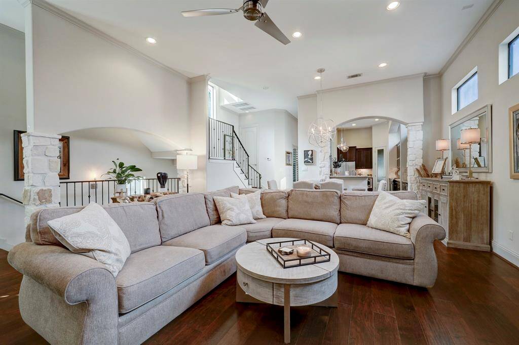 This spacious living area features a cozy sectional sofa, hardwood floors, and abundant natural light. The open layout connects to a modern kitchen and dining space, highlighting elegant lighting and stone accents for a warm, inviting atmosphere.