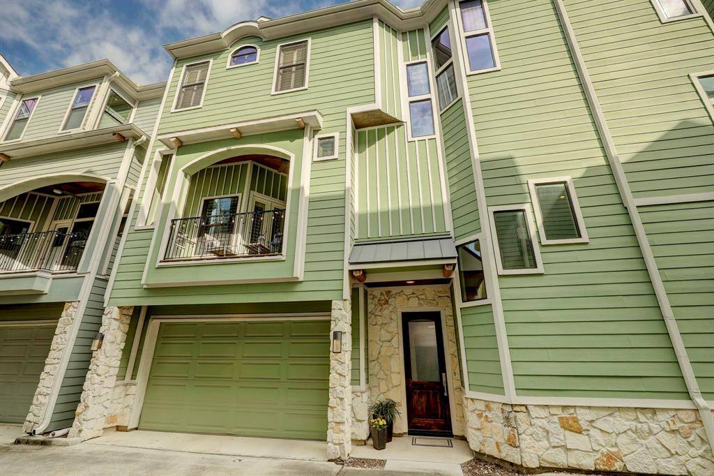 This photo shows a modern, three-story home with a green exterior and stone accents. It features a balcony and a two-car garage, providing a stylish and practical living space.