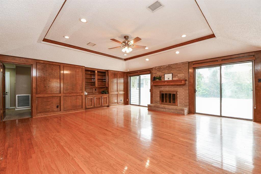 Large family room with build in wood cabinetry, trey ceiling w/ wood accents, wood burning fireplace w/ brick surround and great lighting from double set of sliders.