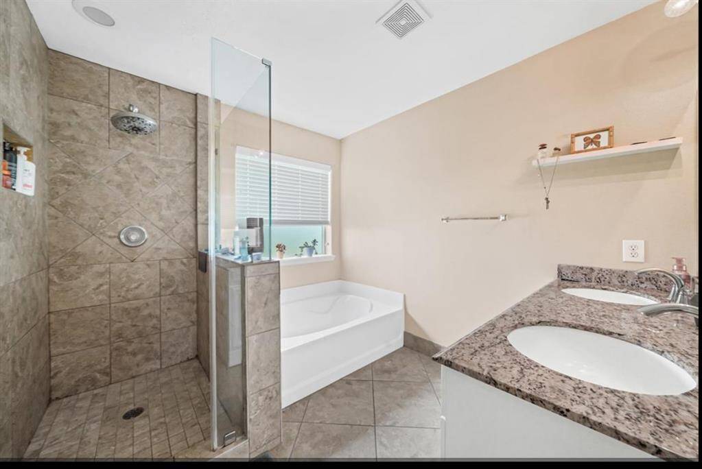 This bathroom features a spacious walk-in shower with modern tile work, a large soaking tub by the window, and a double-sink vanity with granite countertops. The neutral tones and ample natural light create a relaxing atmosphere.