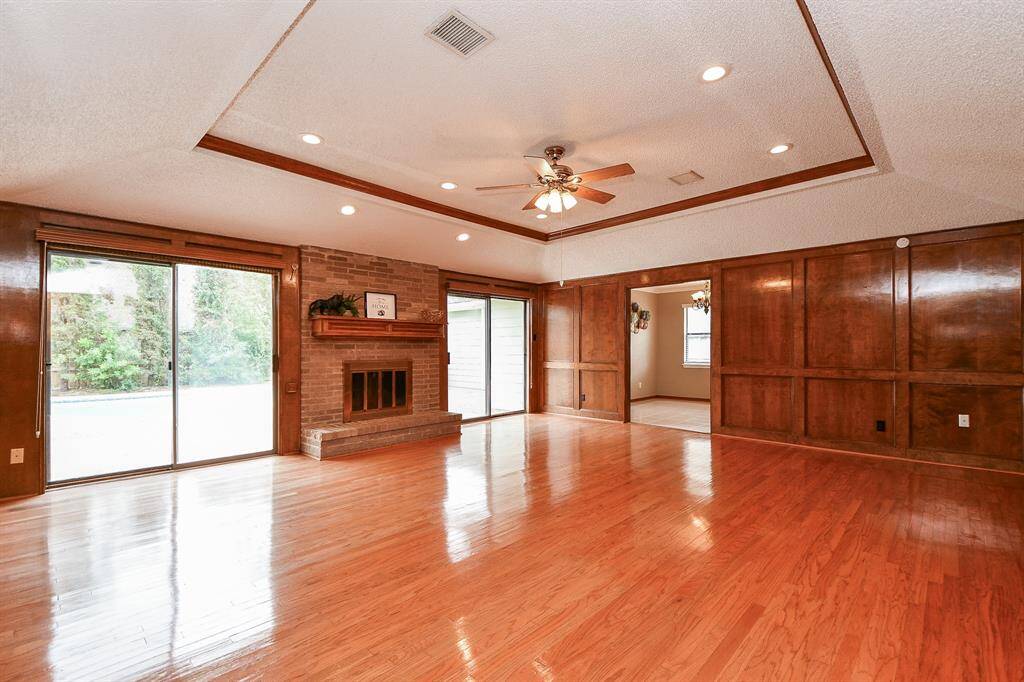 Spacious family room featuring elegant wood paneling, a cozy brick fireplace, and large sliding doors for abundant natural light. Perfect for gatherings and relaxation.