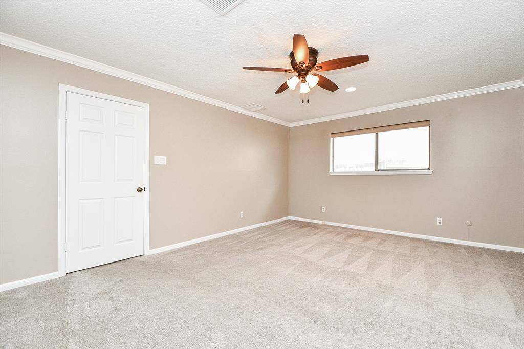 Spacious primary bedroom with modern ceiling fan, soft carpet, and ample natural light.