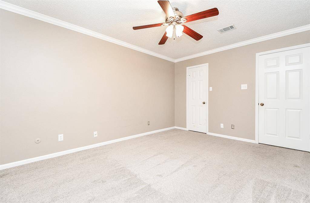 Spacious bedroom with fresh, neutral tones and plush carpeting, featuring a ceiling fan and ample natural light.