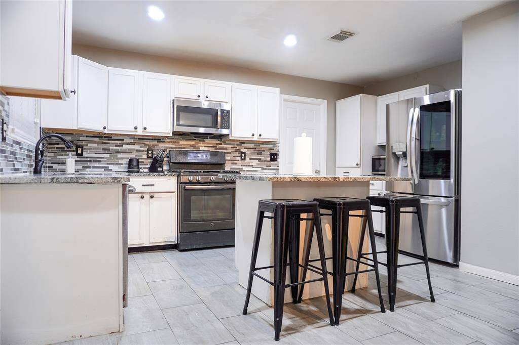Modern kitchen with white cabinets, stainless steel appliances, and a stylish tile backsplash. Features a central island with granite countertops. Bright and spacious layout.