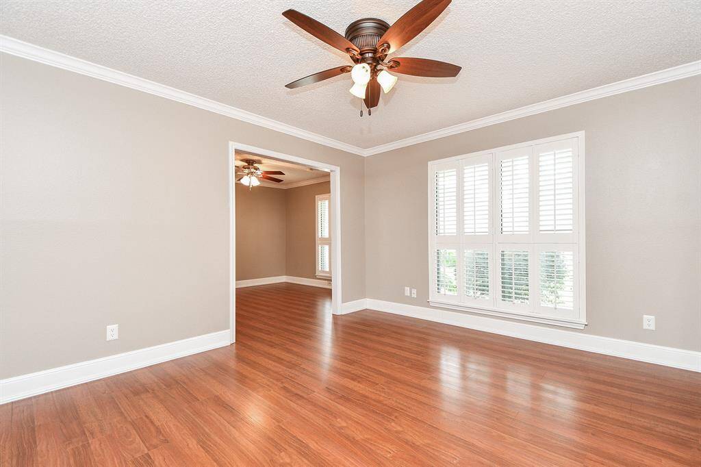 Living Room space w/ rich flooring, neutral paint tones, crown molding accents & plantation shutters.