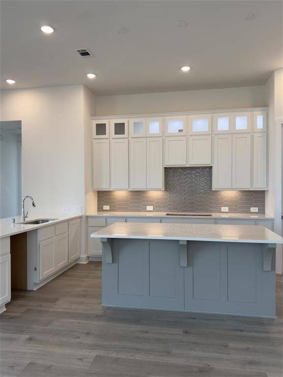 HOME IN PROGRESS - A gourmet kitchen featuring under cabinet lighting, upgraded stacked upper cabinets with glass inserts and puck lights, and a sleek 5-burner gas cooktop!