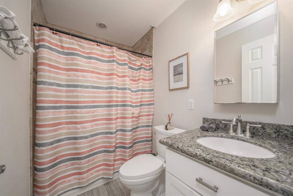This shared bath has been lovingly updated to include wood plank floors, a granite-topped vanity, and a tub and shower combination with tile surround.