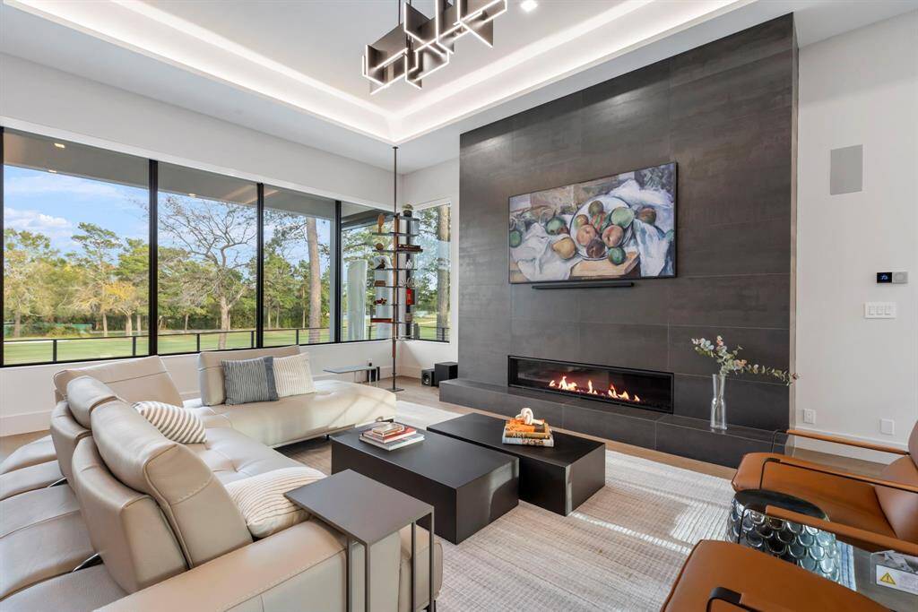 This spacious living room features a modern 12' wide fireplace with a 72" gas log insert.  The large windows offer a scenic golf course view, creating a bright and inviting atmosphere.