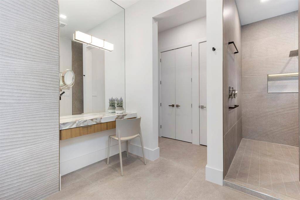 View of the vanity in the primary bathroom.  The entrance to the primary closet has a linen closet and a closet for a stack washer/dryer.  The primary shower is on the right.