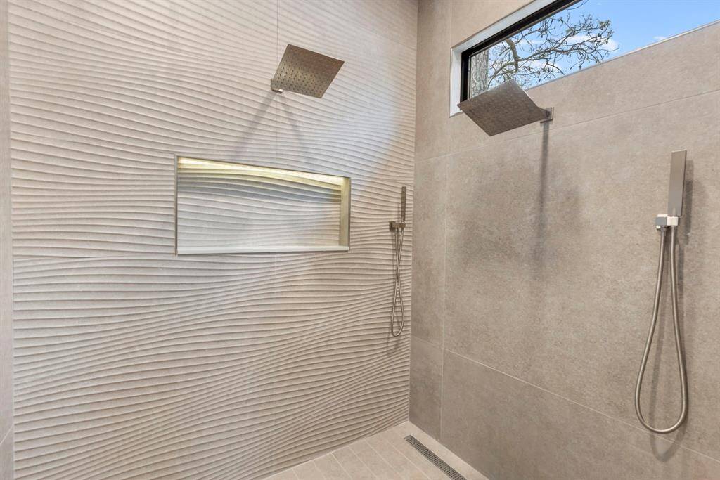 Large oversized primary shower with two shower heads with hand wands, and a rain shower with a backlit shampoo niche and linear drain.