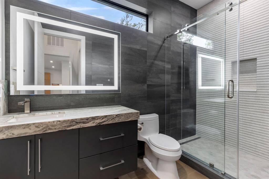The ensuite guest room/study bathroom has tiled walls, large LED mirror, leather finish countertop and 72" window. The walk in shower has a sliding glass door, shampoo niche and a linear drain.