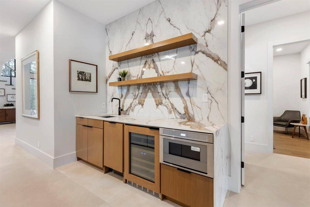 The seller added this bar in the first-floor family/gameroom which has a sink, dishwasher, under-counter refrigerator, a microwave and a beautiful quartz bookmatched backsplash with shelving. The doorway on the right leads to the 2nd bedroom with ensuite pool bathroom.