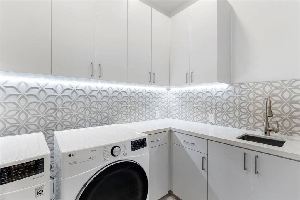 View of the downstairs utility room with under cabinet lighting, sink and lots of storage.