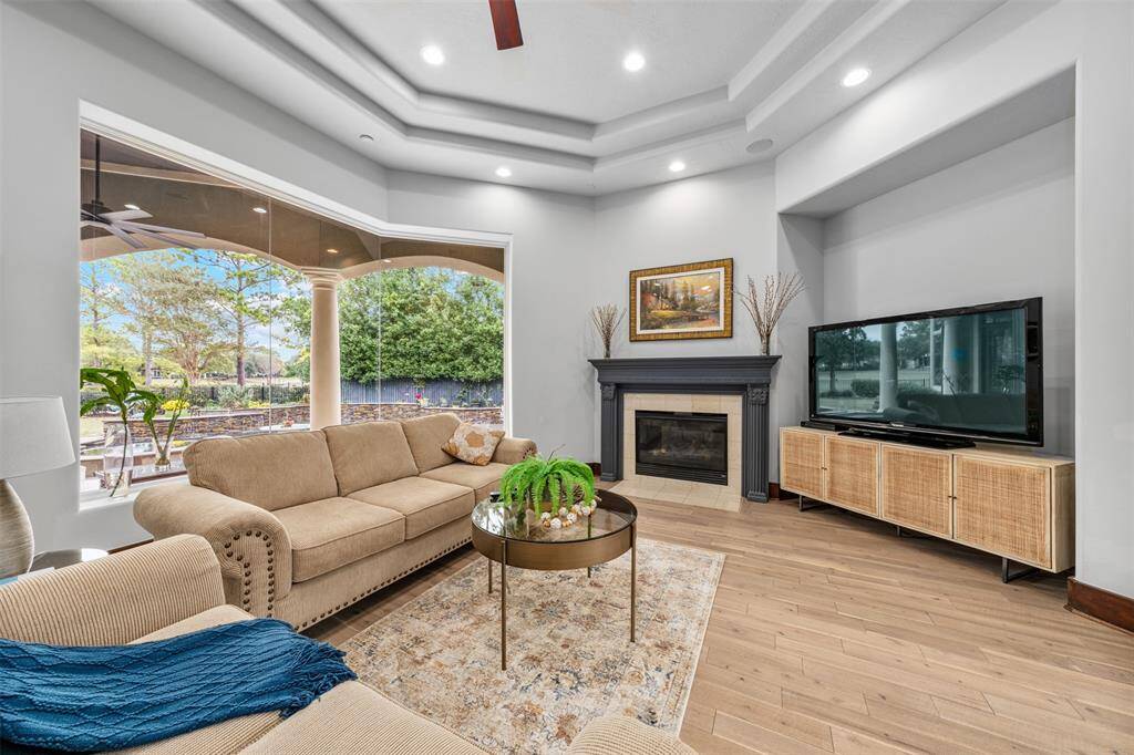 The living room features a breathtaking view of the private backyard pool and golf course, complemented by a modern fireplace that creates a classy ambiance, enhanced by abundant natural light.