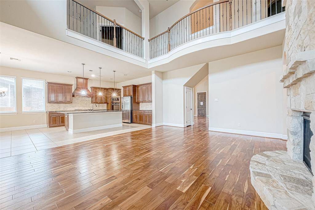 Spacious living area with an open floor plan, high ceilings, and a second-floor balcony. Features hardwood floors, a stone fireplace, and a modern kitchen with an island.