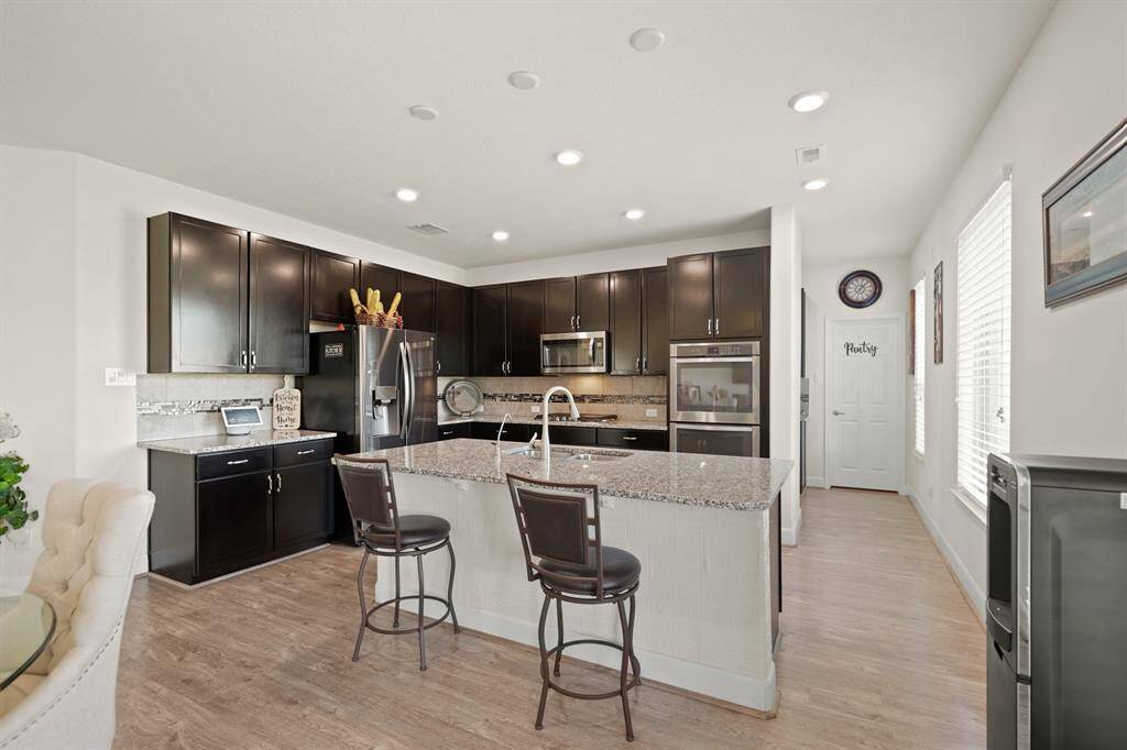 This modern kitchen features granite countertops, stainless steel appliances, dark cabinetry, double ovens, a gas stove, and a spacious island with bar seating. It is perfect for cooking and entertaining!