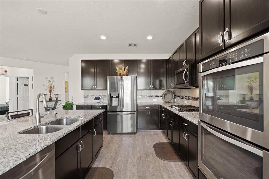 This modern kitchen features granite countertops, stainless steel appliances, dark cabinetry, double ovens, and a spacious island.