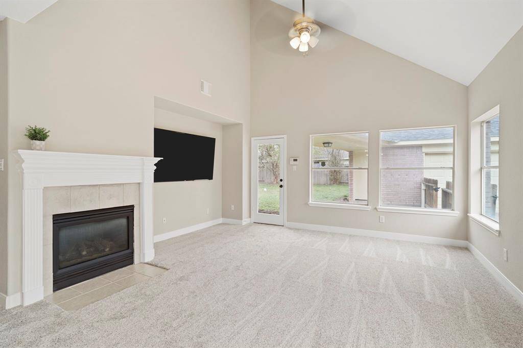 The living room has high ceilings, new plush carpet, high ceilings, ceiling fan, and access to the backyard.