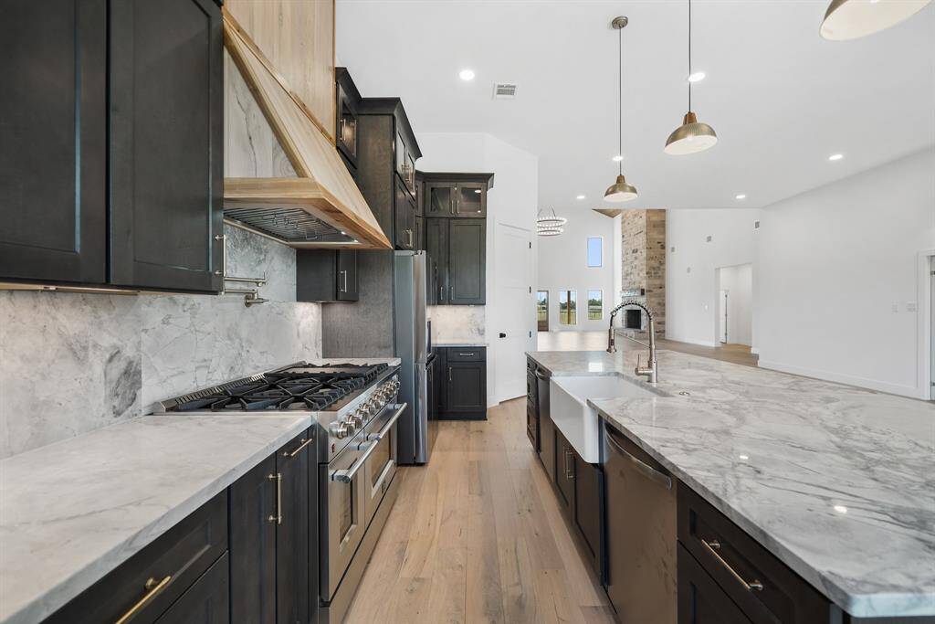 Modern kitchen with sleek dark cabinetry, quartz countertops, and a spacious island with a farmhouse sink. Stainless steel appliances and pendant lighting add a touch of elegance, while the open layout seamlessly connects to the living area.