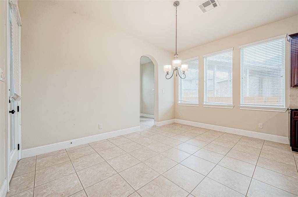 Bright dining area with tile flooring, neutral walls, and ample natural light from multiple windows. Features a stylish light fixture and an arched doorway leading to another room.