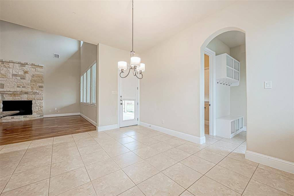 This stunning living area boasts soaring ceilings, a dazzling modern chandelier, and a warm stone fireplace. Large windows flood the space with natural light, while sleek tile flooring and thoughtful storage nooks enhance its elegance.