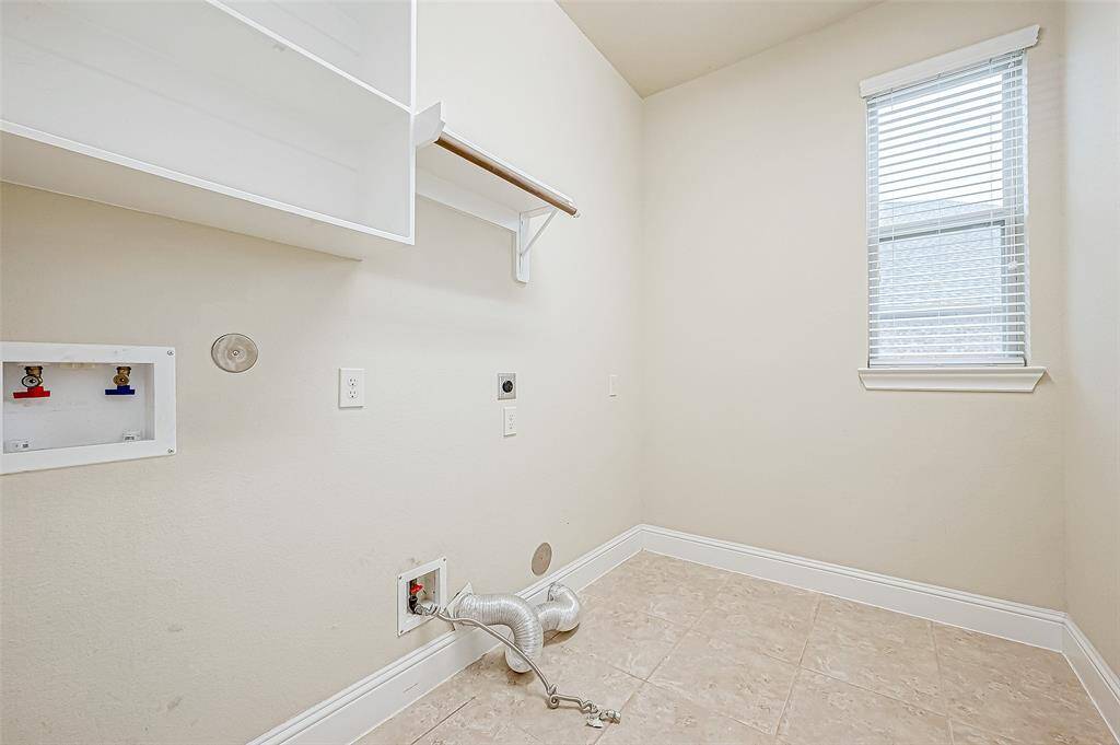 Bright, spacious laundry room featuring tiled flooring, built-in shelving, and a window for natural light. It has hookups for a washer and dryer and a utility shelf for storage.