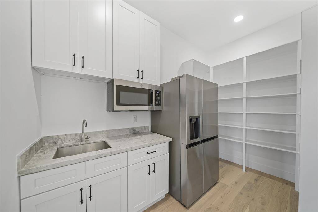 Butler's pantry with white cabinetry, a stainless-steel refrigerator, a built-in microwave, and open shelving. Offering a clean and functional space.