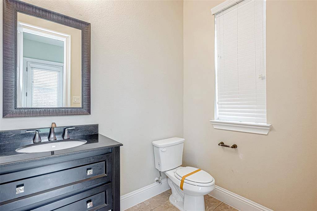 This bathroom features a modern vanity with a dark countertop, a large framed mirror, and a window with blinds. The neutral color palette and clean design create a bright and inviting space.