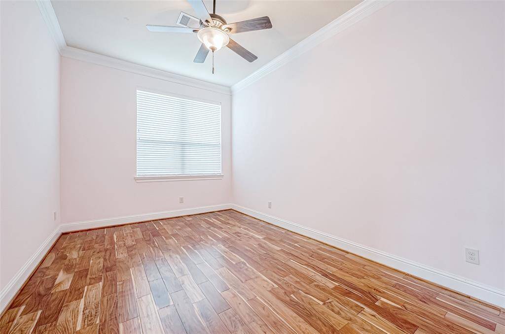 Bright room with hardwood floors, a ceiling fan, and a large window with blinds, perfect for a bedroom or office space.