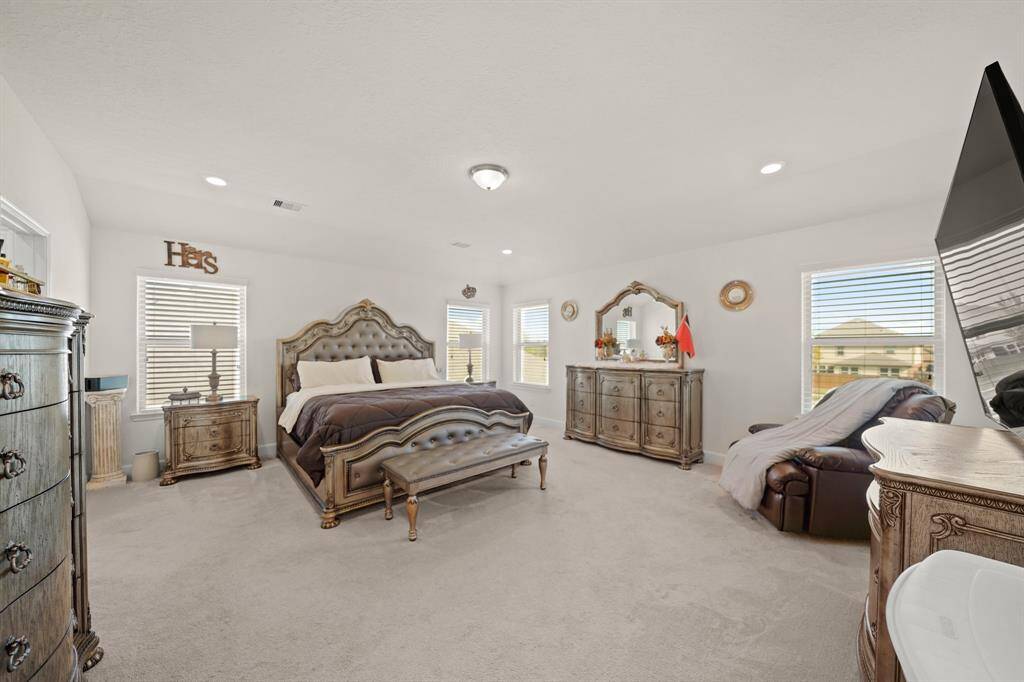 This elegant primary bedroom upstairs has ample natural light, plush carpeting, and luxurious furnishings, creating a serene and spacious retreat.