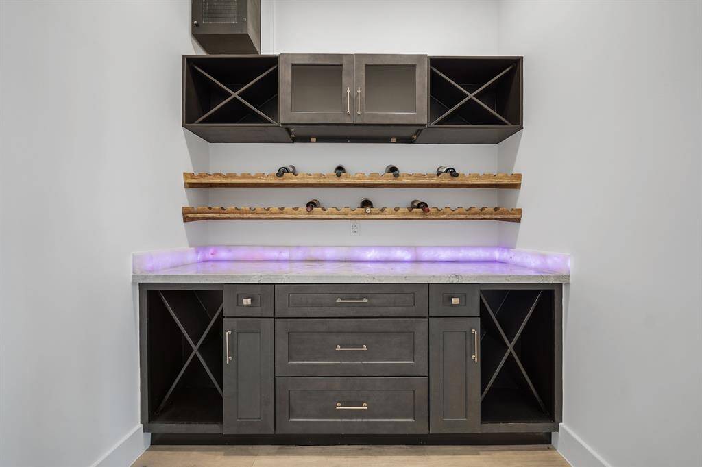 Sleek home bar inside the chilled room offering dark cabinetry, wine racks, and open shelving. The countertop features modern LED lighting, making it a stylish and functional space.