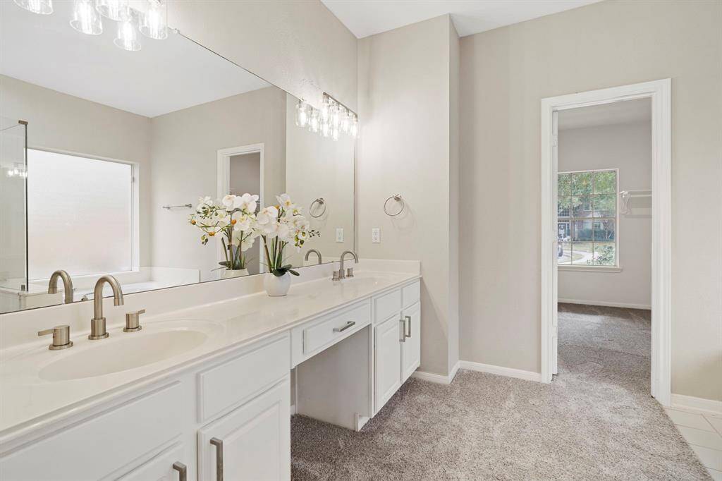 The primary bathroom featuresplush new carpet, dual sinks, and vanity area.