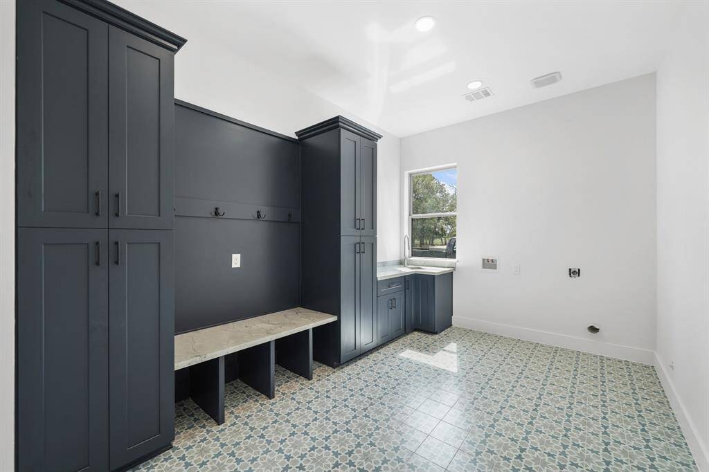 Utility room offers a built-in bench, sink, and patterned tile flooring. A window provides natural light, and there’s ample storage and workspace.