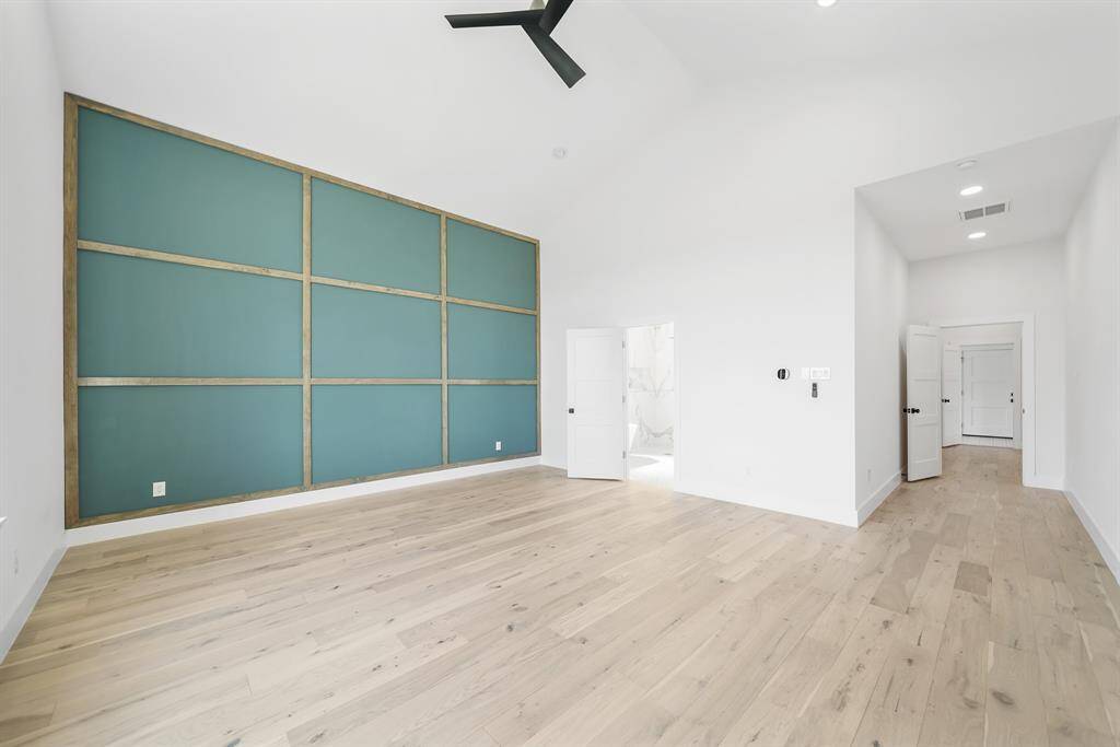 Light-filled room with natural wood flooring and a stylish accent wall. High ceilings and modern fixtures enhance the open, airy feel.