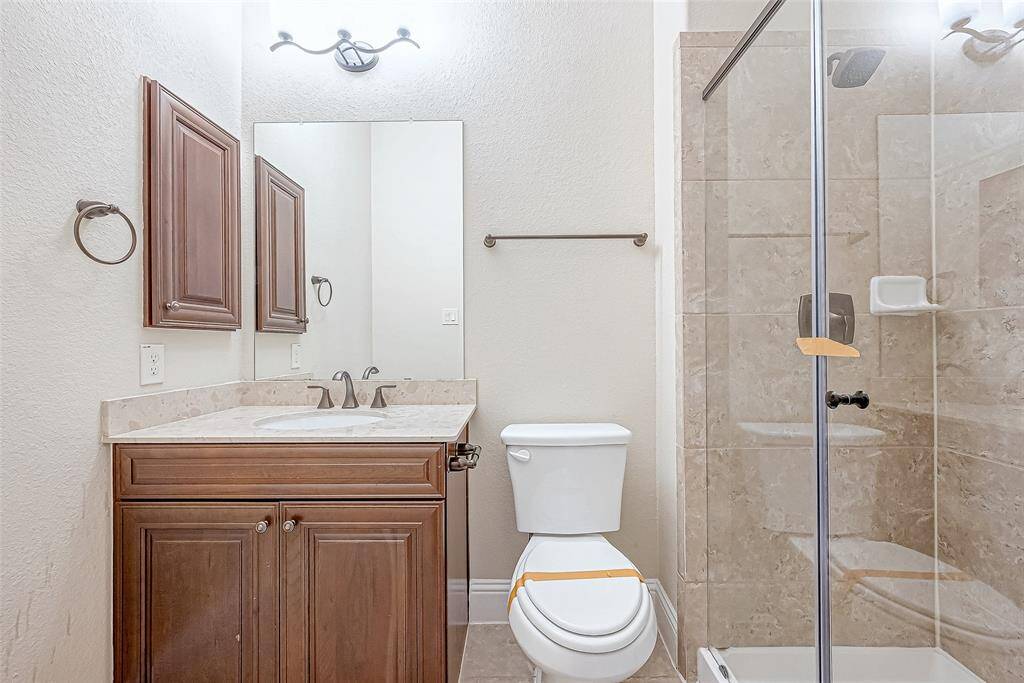 This bathroom features a modern design with a glass-enclosed shower, a sleek vanity with a marble countertop, and warm wood cabinetry, complemented by neutral tile and wall colors.