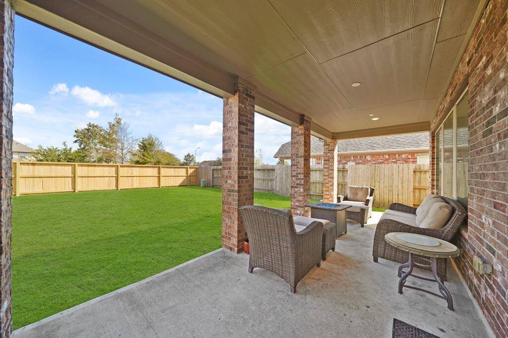 The covered patio with ample seating space overlooking a spacious, fenced backyard is perfect for outdoor entertaining and relaxation.