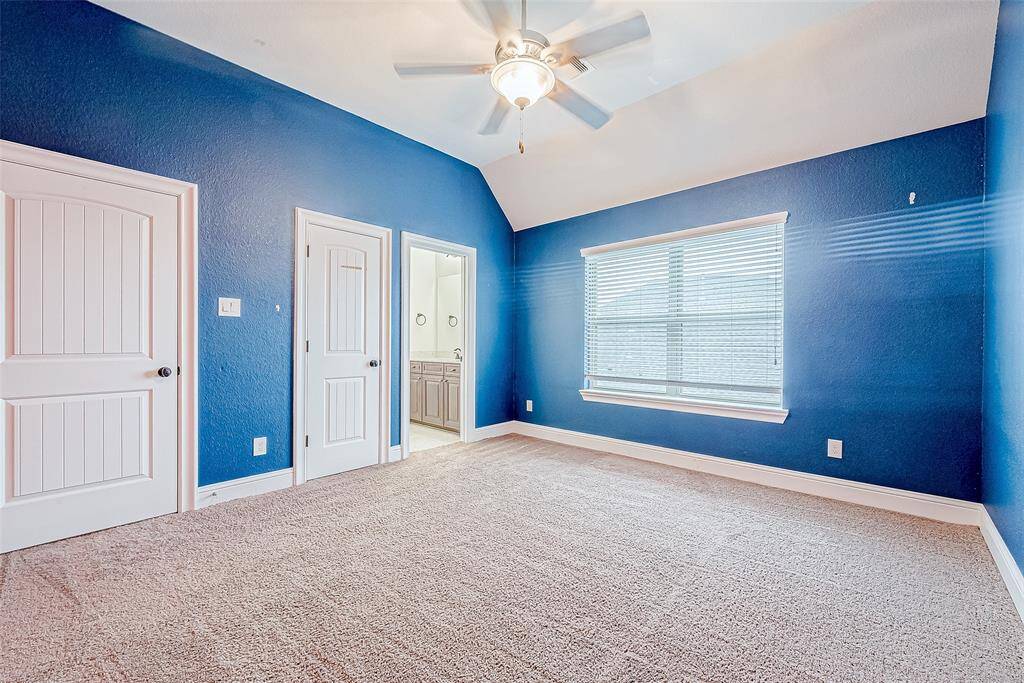 Elevate your rest in this stylish bedroom, featuring bold blue hues, soft carpet, and ample sunlight. Modern amenities include a ceiling fan and sleek bathroom access.