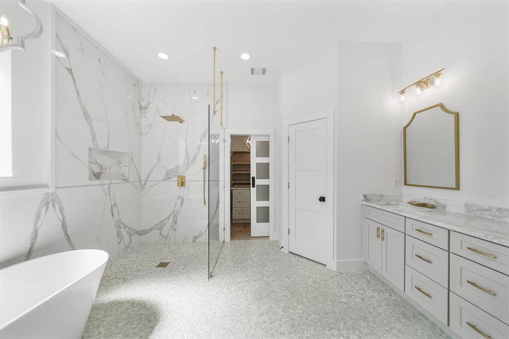 Primary bathroom features a spacious, modern design with a glass shower, elegant marble tiles, a freestanding bathtub, and sleek cabinetry.