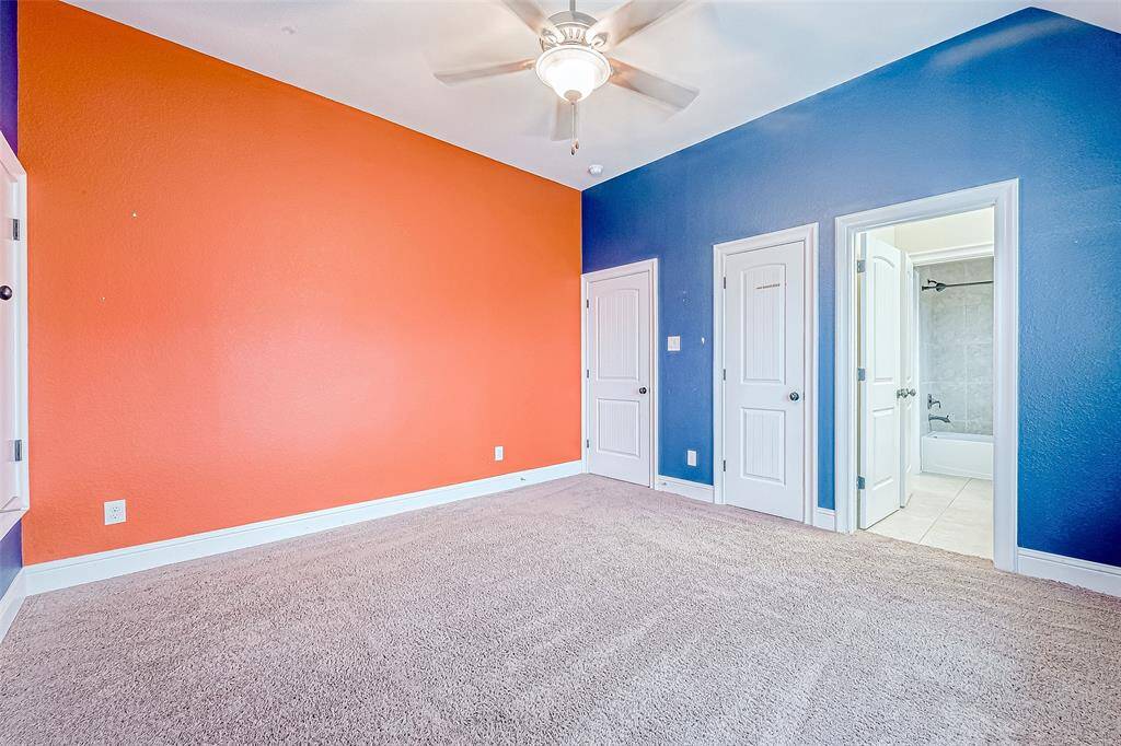 Bright bedroom with bold orange and blue accent walls, carpeted flooring, a ceiling fan, and access to an en-suite bathroom.