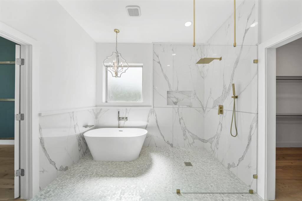 Freestanding bathtub, elegant marble walls, and a spacious glass shower. It also includes stylish gold fixtures and a large, frosted window for natural light.