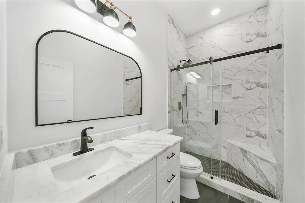 This modern bathroom features a sleek design with a large marble vanity, black fixtures, and a spacious glass-enclosed shower with elegant tile work.