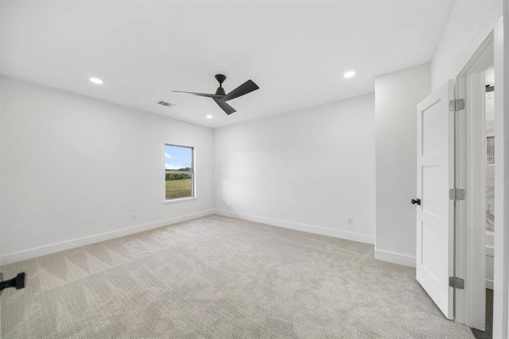 Bright and spacious upstairs bedroom with neutral walls and carpet, a modern ceiling fan, and a window offering a scenic view. The room features recessed lighting and an attached bathroom.